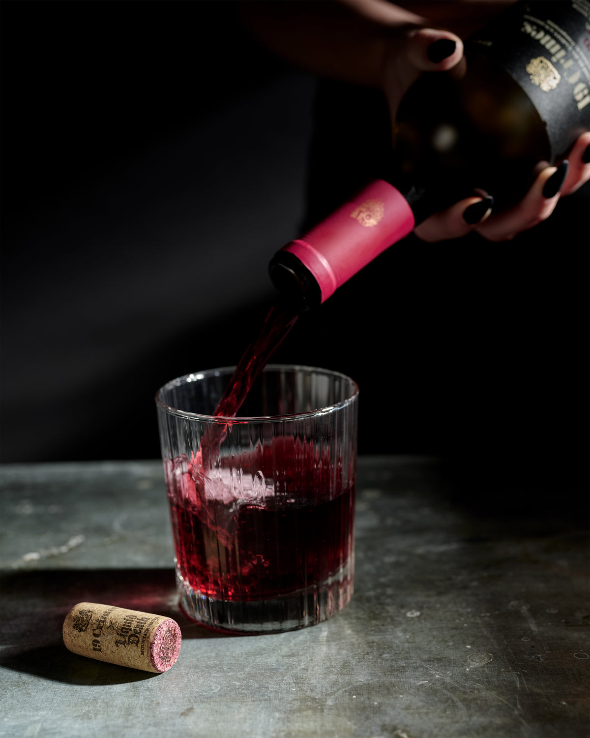 Red wine being poured into a glass with a bottle and cork on a dark surface