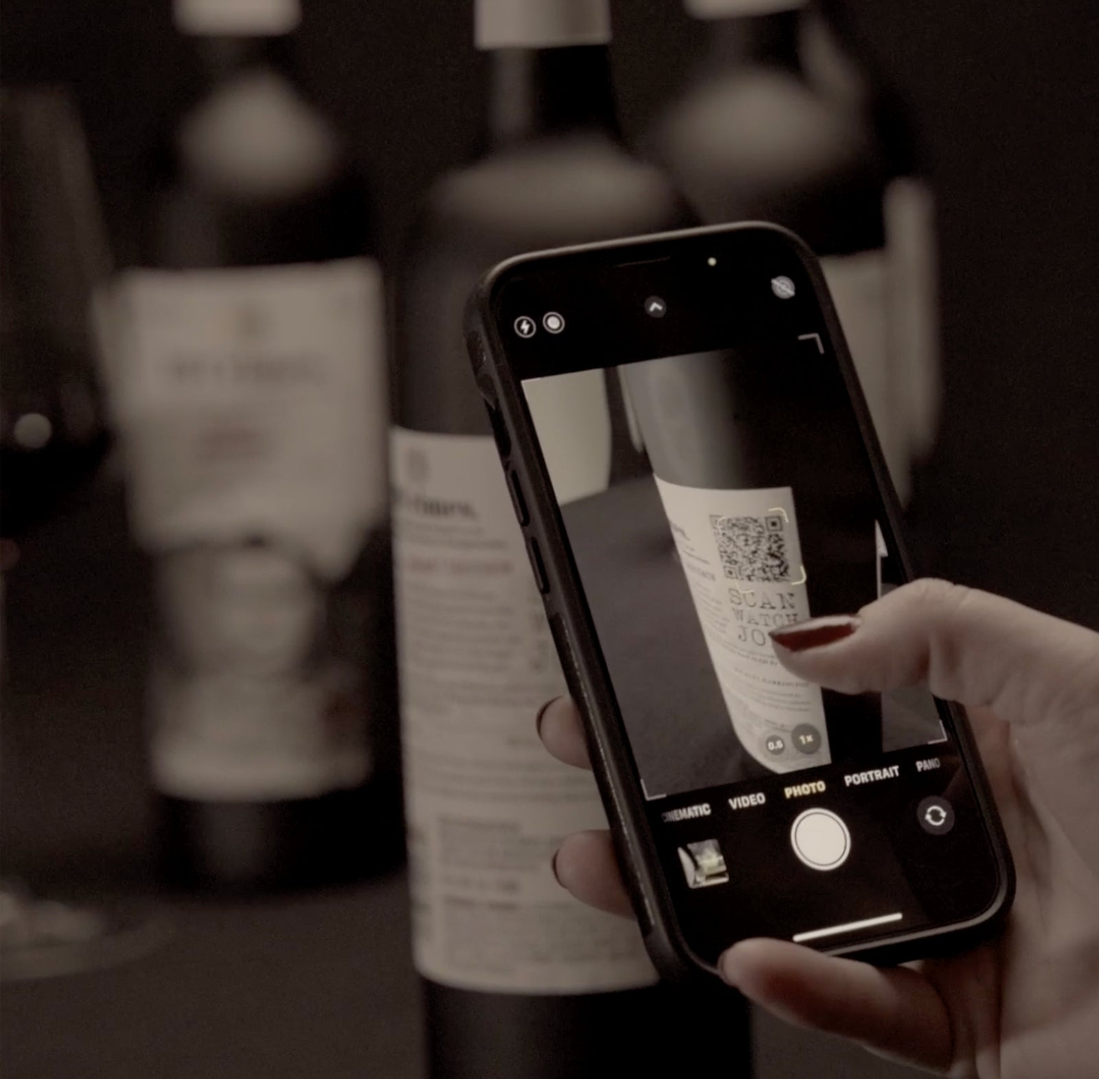 Screenshot of "How to" video. A hand holding a phone in camera mode scanning a QR code