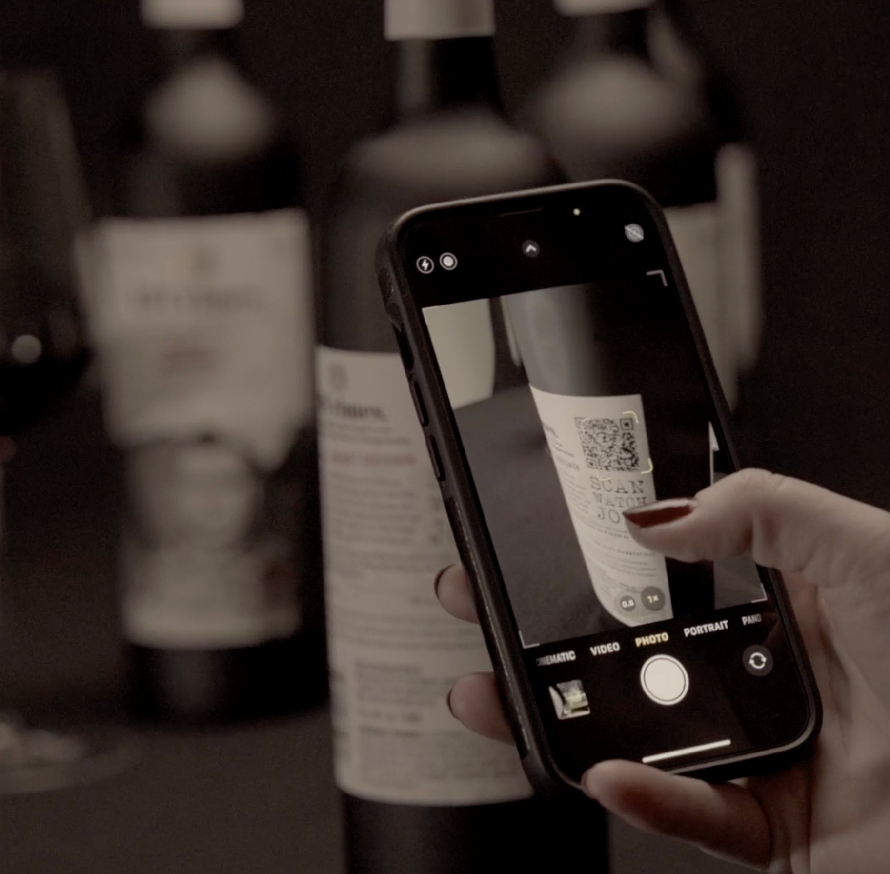 Screenshot of "How to" video. A hand holding a phone in camera mode scanning a QR code